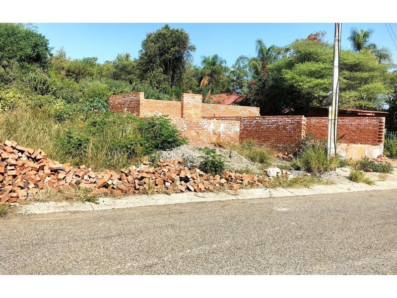 A vacant residential plot featuring partial brick boundary walls, overgrown vegetation, and construction debris, offering a blank canvas for future development.