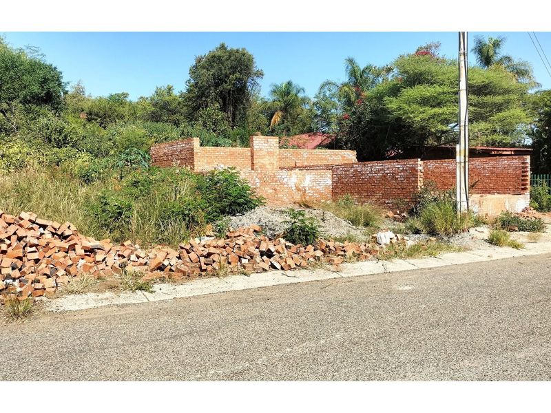 A vacant residential plot featuring partial brick wall construction, loose building materials, and established vegetation, offering a blank canvas for development.