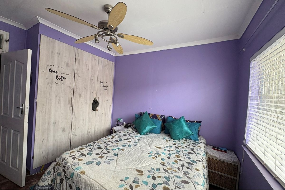 A bedroom featuring built-in wooden wardrobes, a ceiling fan, and a window with fitted blinds.