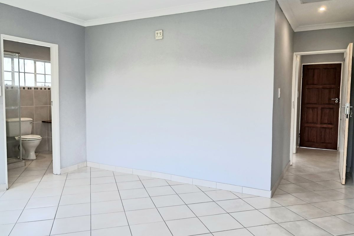 An empty living area featuring neutral tiled flooring, coved ceilings, and access to an adjacent bathroom and secondary room.