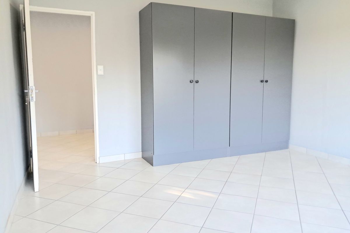 A clean, empty bedroom featuring neutral tiled flooring and modern grey built-in cupboards, offering a versatile space ready for personalization.