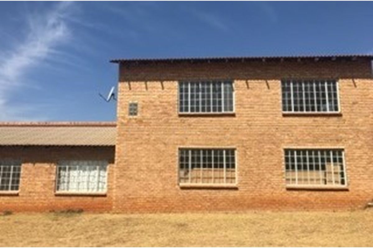 A two-story exposed brick farmhouse exterior featuring steel-framed windows and a tiled roof, set against a clear sky.