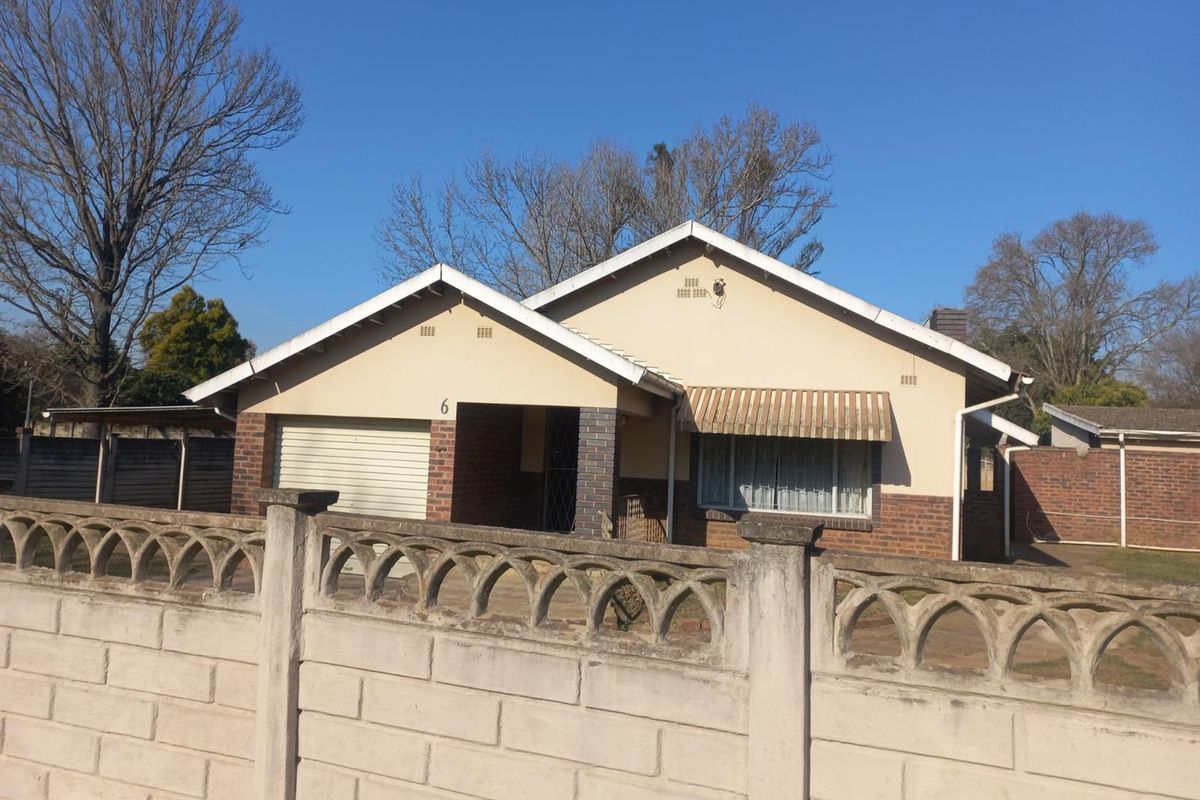 Front view of a single-story brick house featuring a roller garage door, tiled roof, and a decorative concrete boundary wall.