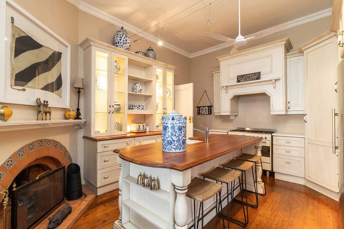 A charming kitchen featuring custom cabinetry, a central island with a wooden countertop, a built-in stove, and a decorative fireplace.