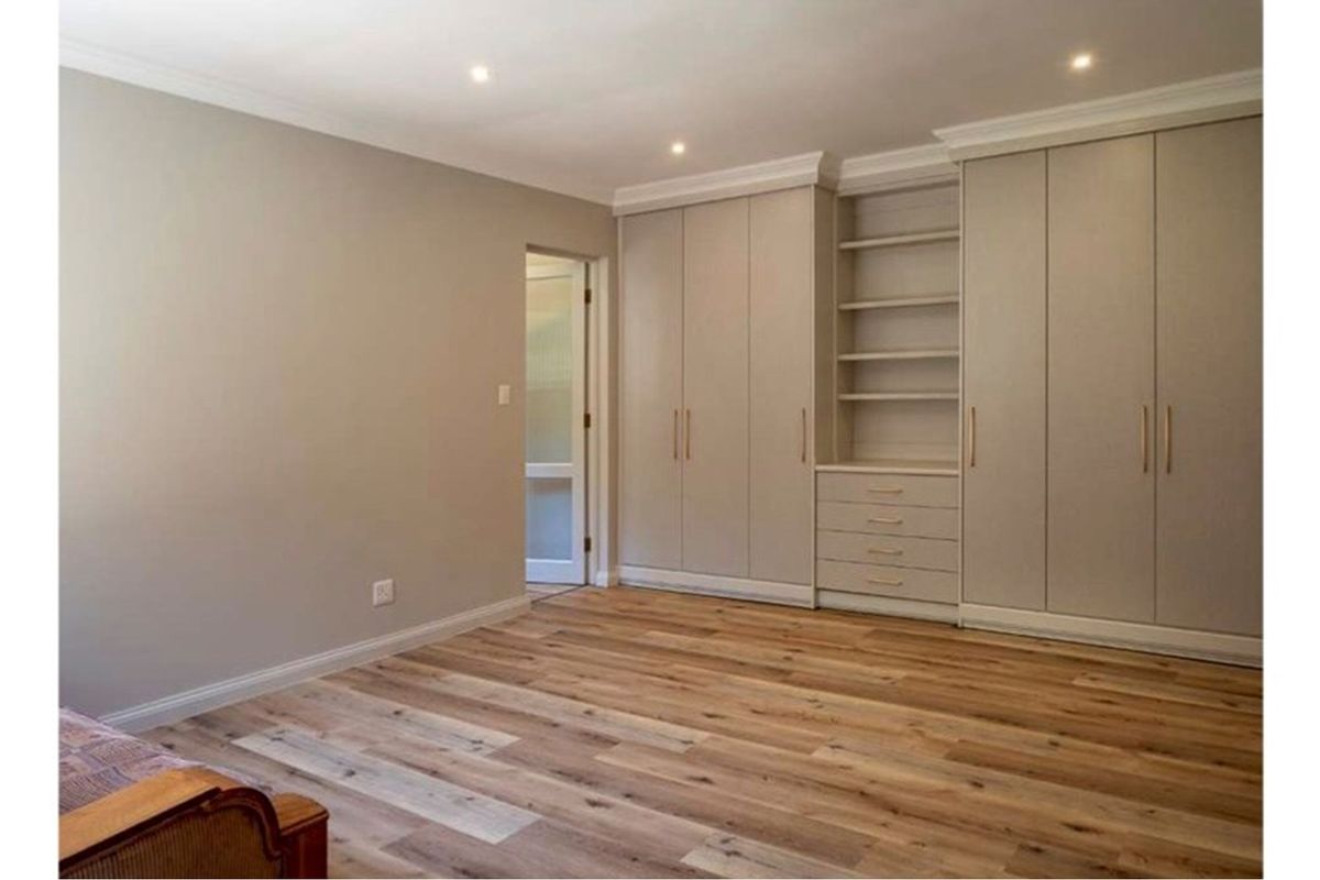 A well-maintained bedroom featuring modern wood-look flooring, recessed ceiling lighting, and extensive built-in cabinetry with integrated shelving and drawers.