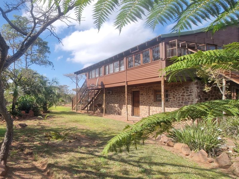 A rustic two-story house featuring stone masonry on the ground floor and timber cladding on the upper level, set within a natural garden.