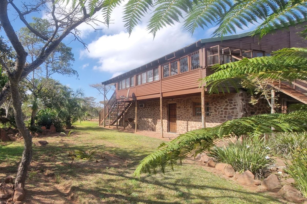 A rustic two-story house featuring stone masonry on the ground floor and timber cladding on the upper level, set within a natural garden.