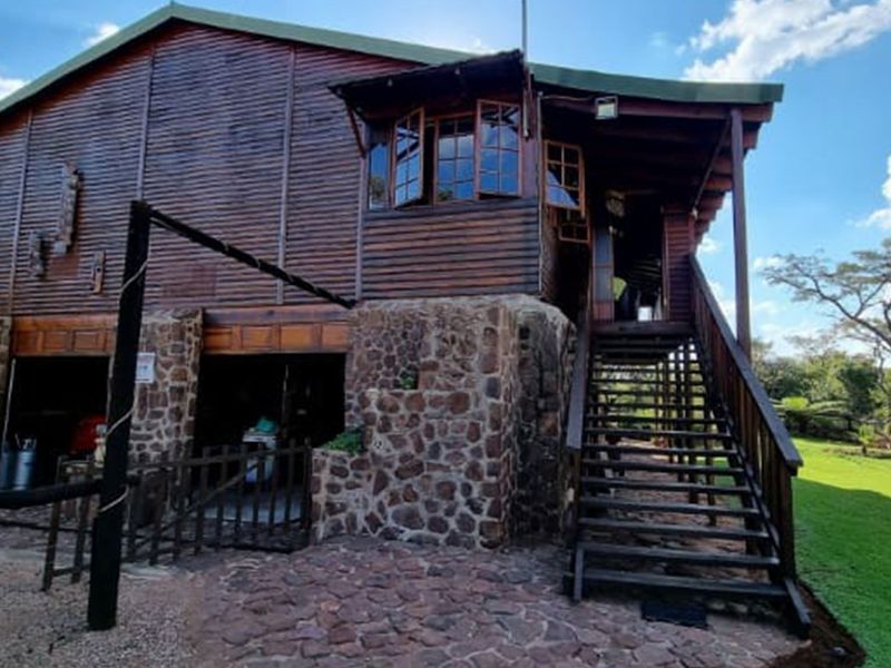 A rustic timber-clad house featuring stone masonry foundations, an elevated wooden staircase, and a covered entrance area set within a landscaped garden.