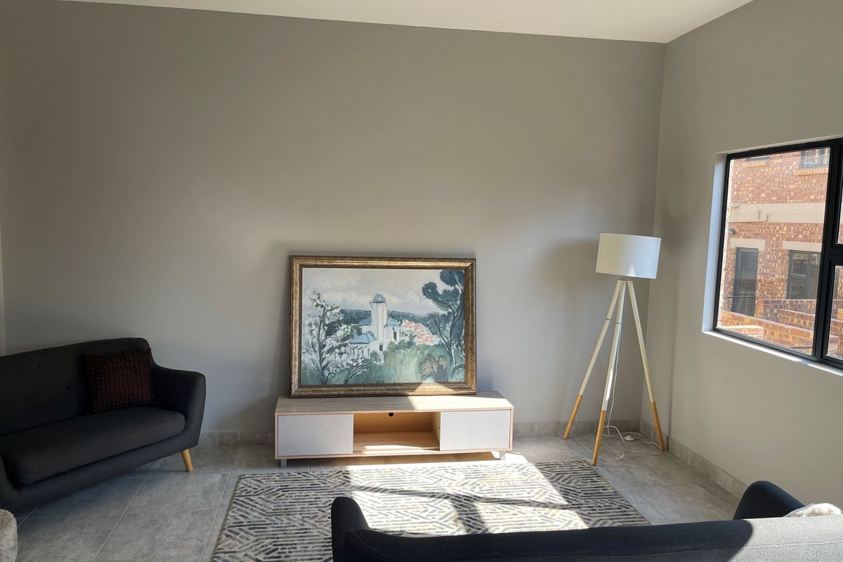A bright living room featuring neutral wall tones, tiled flooring, and a large window allowing for natural light.