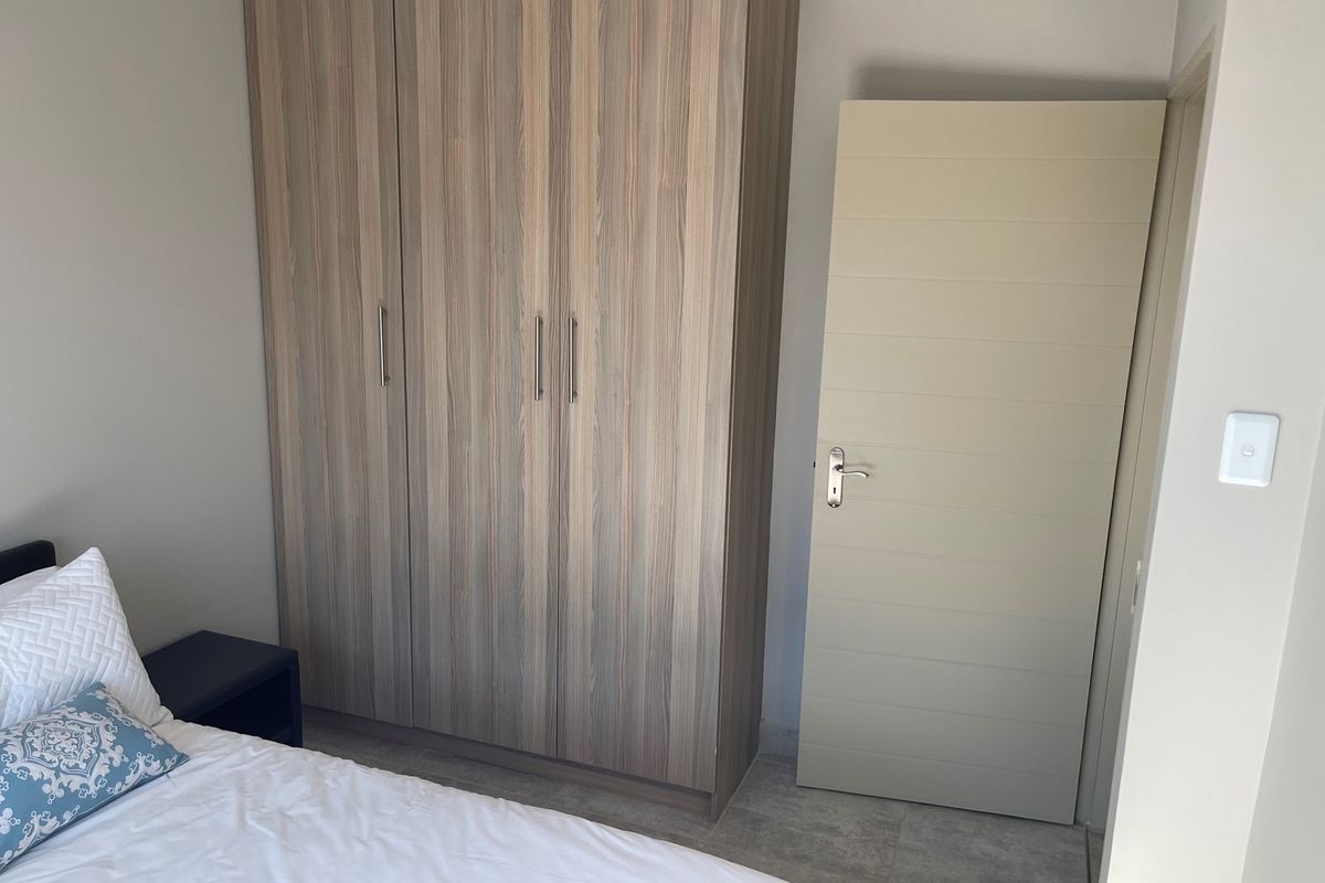 A bedroom featuring built-in wood-grain cabinetry and a modern horizontal-panel interior door, finished with neutral wall tones and tiled flooring.