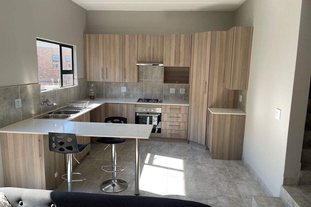Modern kitchen featuring wood-look cabinetry, stone countertops, a built-in oven, gas hob, extractor fan, and a breakfast nook with tiled flooring.