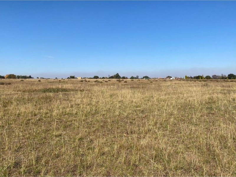 A wide, open view of a vacant residential plot featuring natural grass and clear horizon lines.