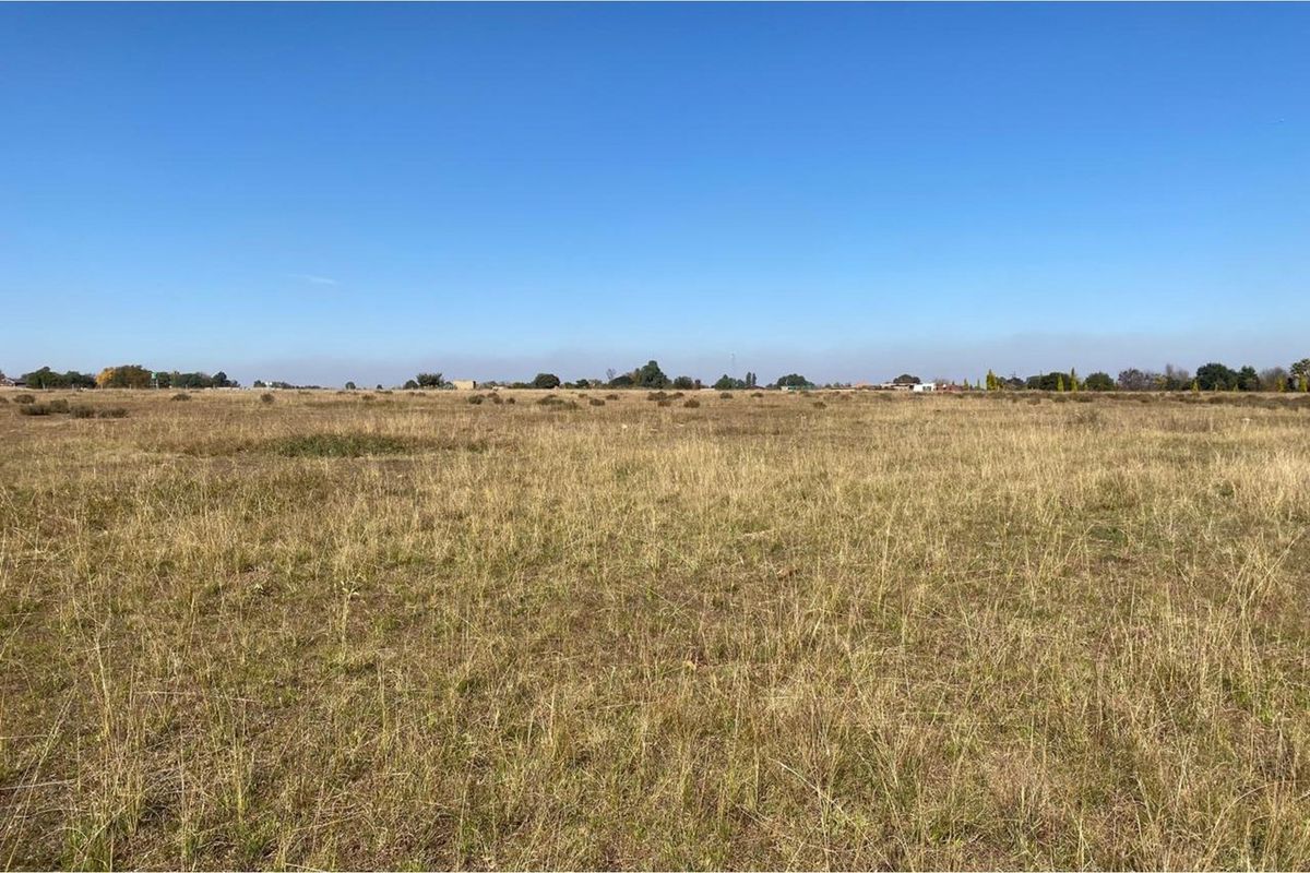 A wide, open view of a vacant residential plot featuring natural grass and clear horizon lines.