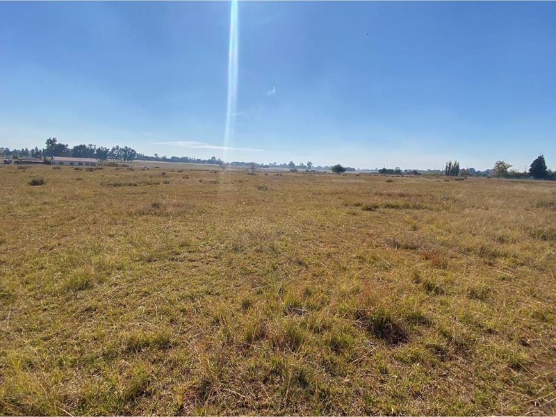 A wide-angle view of a large, open residential vacant land plot featuring natural grassland under a clear blue sky.