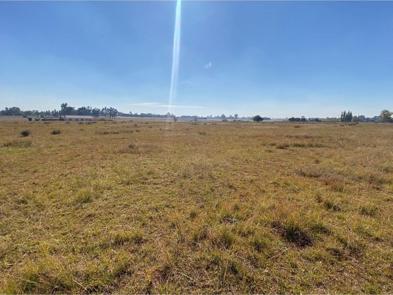 A wide, open expanse of vacant residential land featuring natural grass coverage and distant horizon views under a clear blue sky.