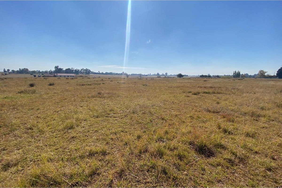 A wide, open expanse of vacant residential land featuring natural grass coverage and distant horizon views under a clear blue sky.
