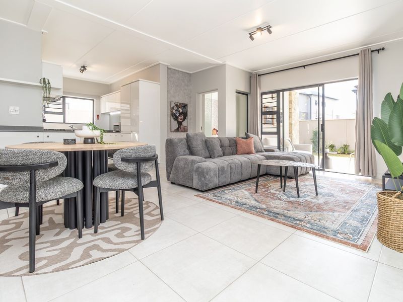 Modern open-plan living and dining area featuring tiled flooring, neutral finishes, and large sliding doors providing seamless access to the outdoor patio space.