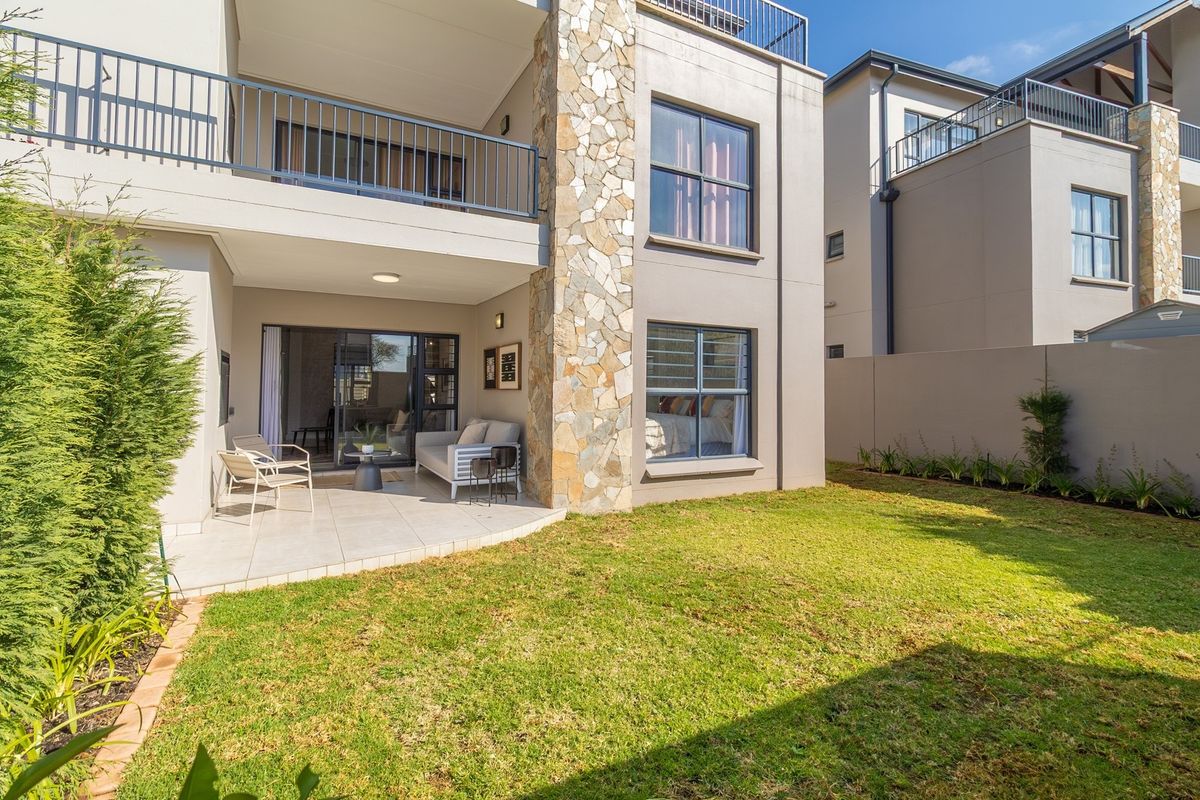 A view of the rear exterior featuring a covered patio with tiled flooring, stone-clad pillar, and a private garden area.