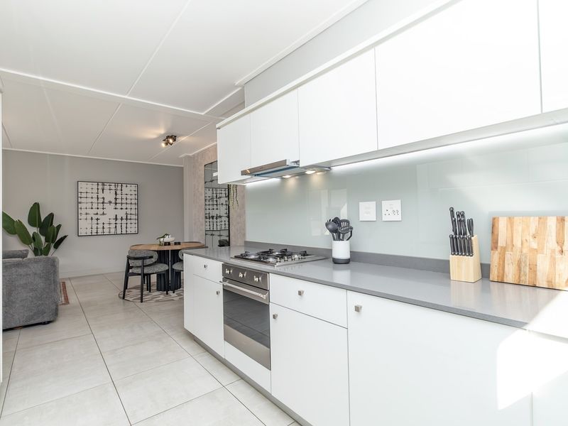 Modern open-plan kitchen featuring sleek white cabinetry, stone countertops, integrated gas hob, and oven, flowing seamlessly into the adjacent dining and living area.