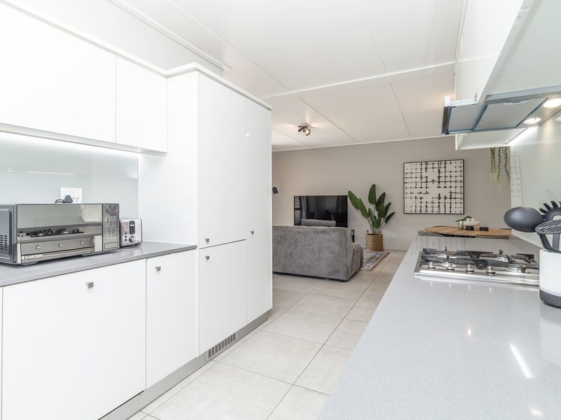 Modern open-plan kitchen featuring sleek white cabinetry, stone countertops, a built-in gas hob, and an integrated extractor fan, flowing into the living area.