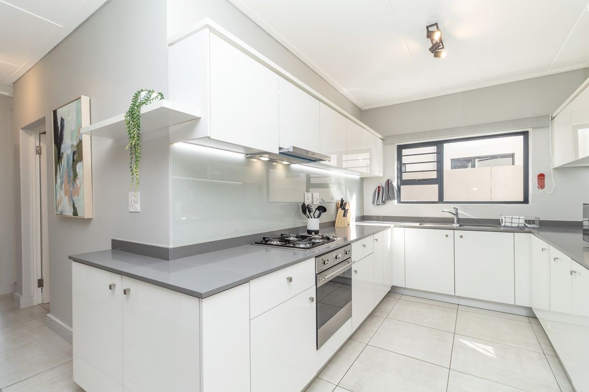 Modern kitchen featuring white high-gloss cabinetry, grey stone countertops, integrated gas hob, built-in oven, extractor fan, and tiled flooring.