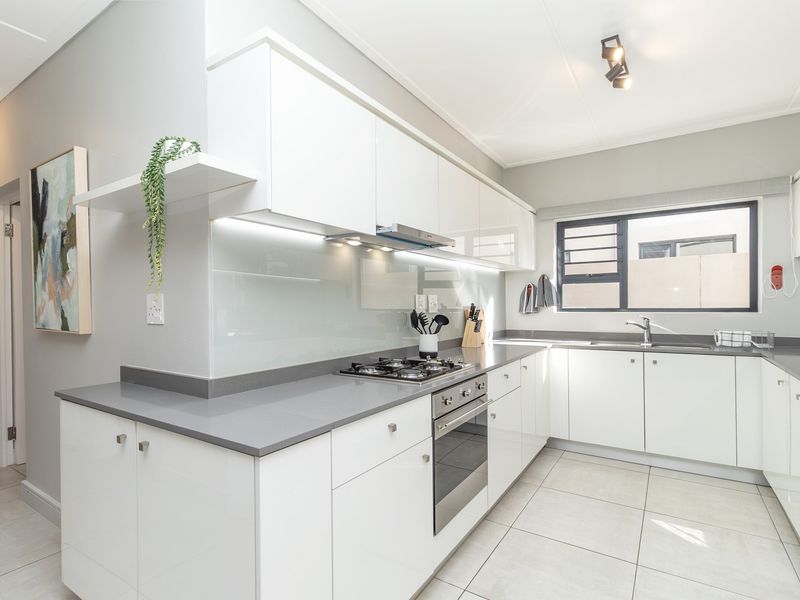 Modern kitchen featuring white high-gloss cabinetry, grey stone countertops, integrated gas hob, built-in oven, extractor fan, and tiled flooring.