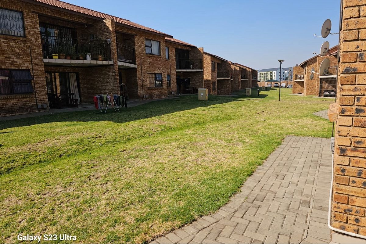 Exterior view of a brick apartment complex featuring shared green space, paved walkways, and private balconies.