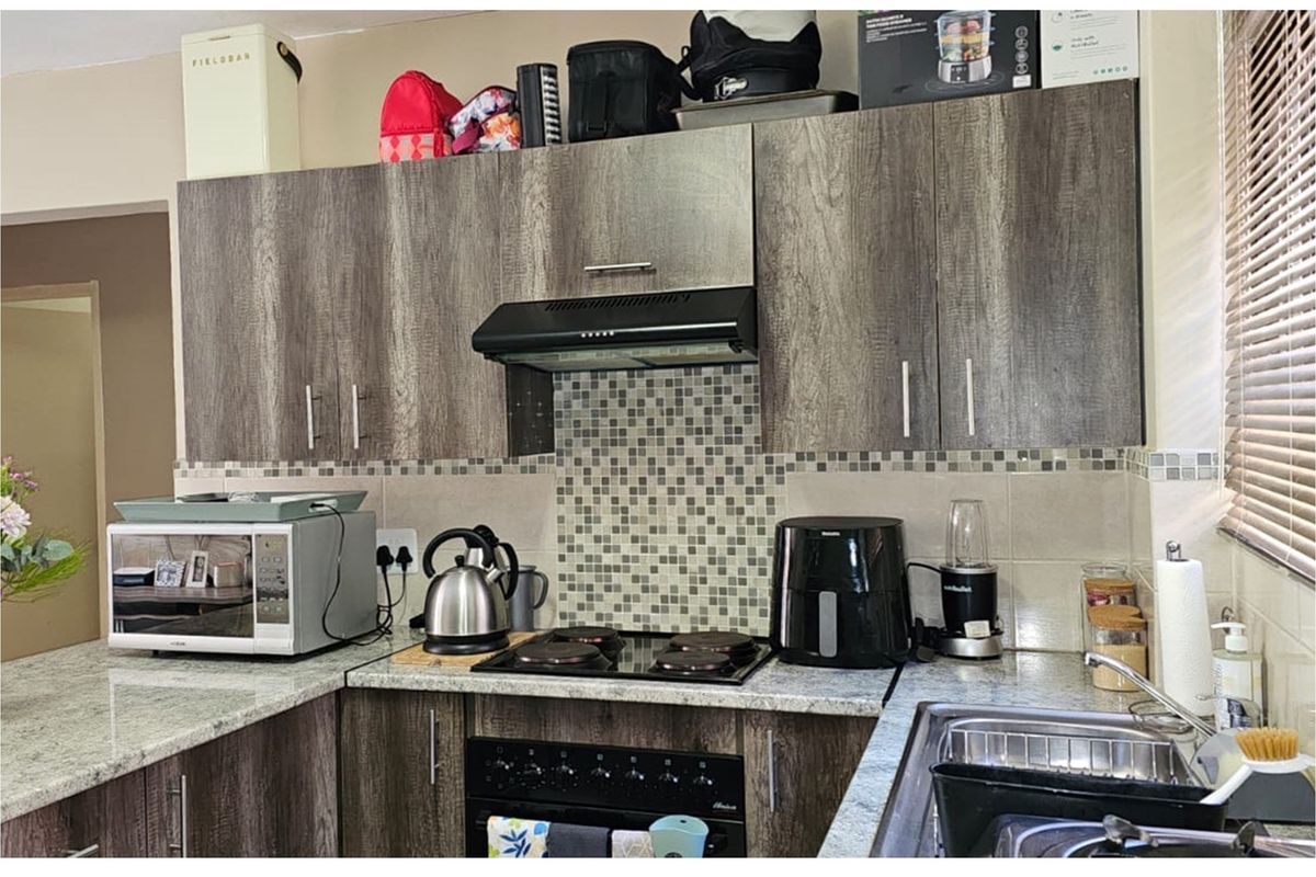 A functional kitchen featuring wood-grain cabinetry, granite countertops, a mosaic tile backsplash, and a built-in oven with an extractor fan.