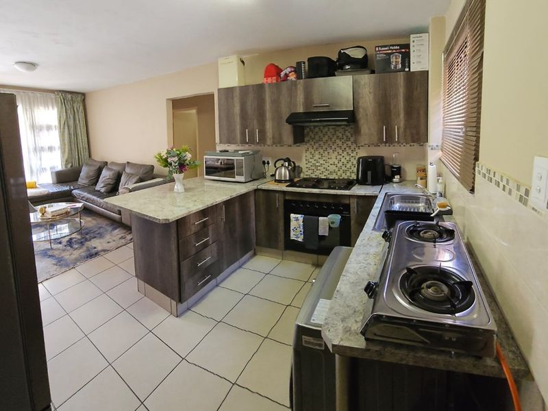 Open-plan kitchen featuring dark wood-look cabinetry, granite countertops, mosaic tile backsplash, and integrated cooking appliances, flowing into the adjacent living area.