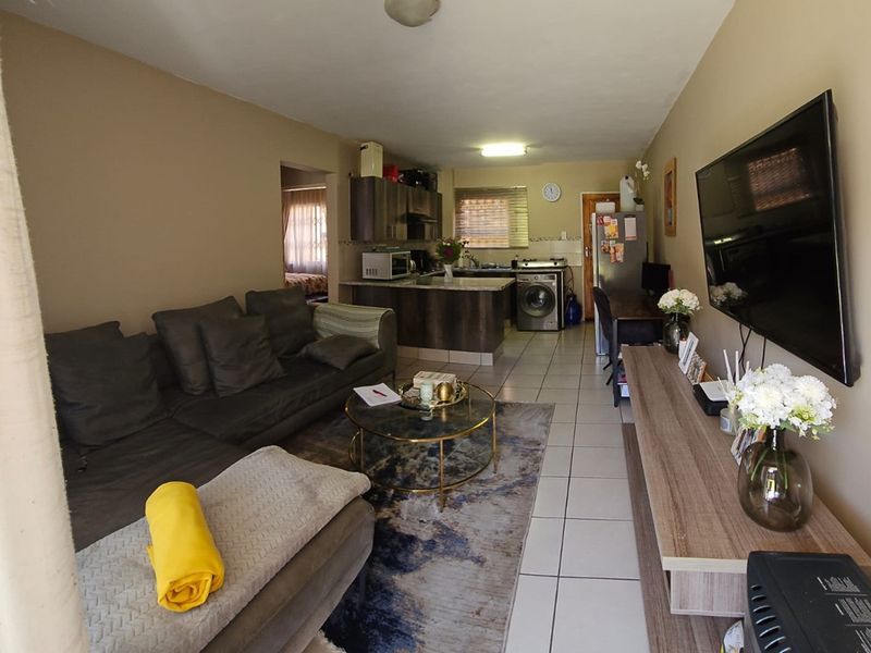 Open-plan living area featuring tiled flooring and a compact kitchen with built-in cabinetry, seamlessly connecting to the lounge space.