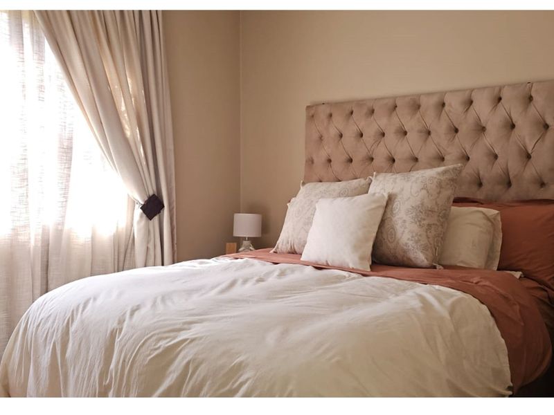 A cozy bedroom featuring neutral wall tones and natural light filtering through window treatments.