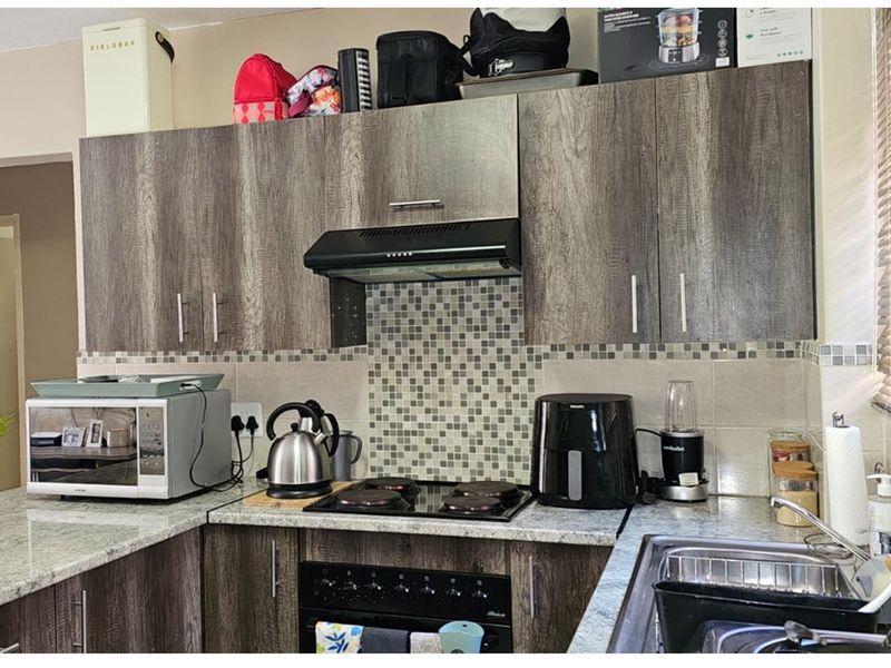 A functional kitchen featuring wood-grain cabinetry, granite countertops, a mosaic tile backsplash, and a built-in oven with an extractor fan.