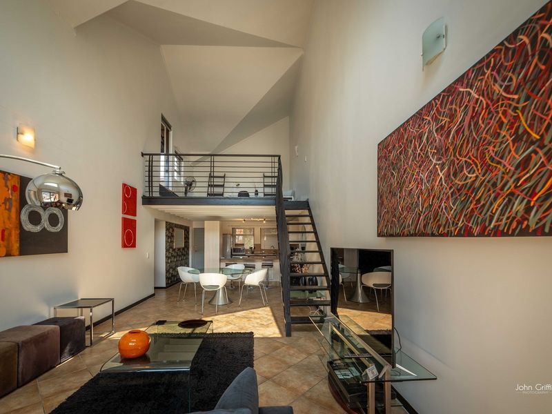 Spacious open-plan living area featuring a mezzanine level, high vaulted ceilings, tiled flooring, and a modern metal staircase.