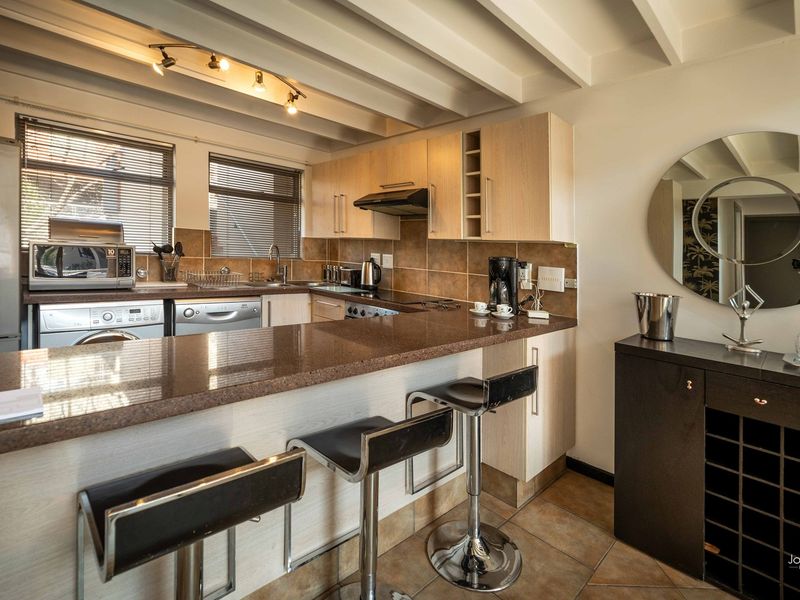 A functional kitchen featuring granite countertops, light wood cabinetry, tiled backsplash, and exposed ceiling beams, with an integrated breakfast bar area.