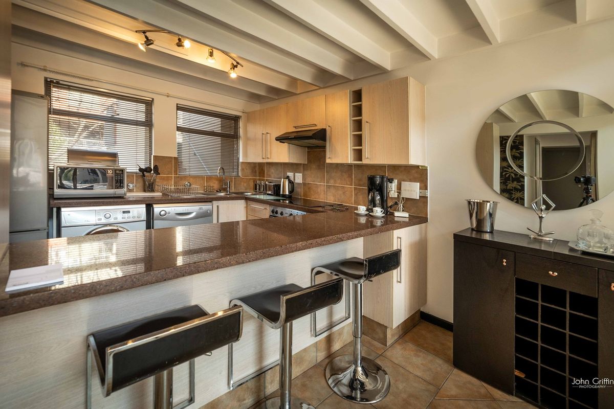 A functional kitchen featuring granite countertops, light wood cabinetry, tiled backsplash, and exposed ceiling beams, with an integrated breakfast bar area.