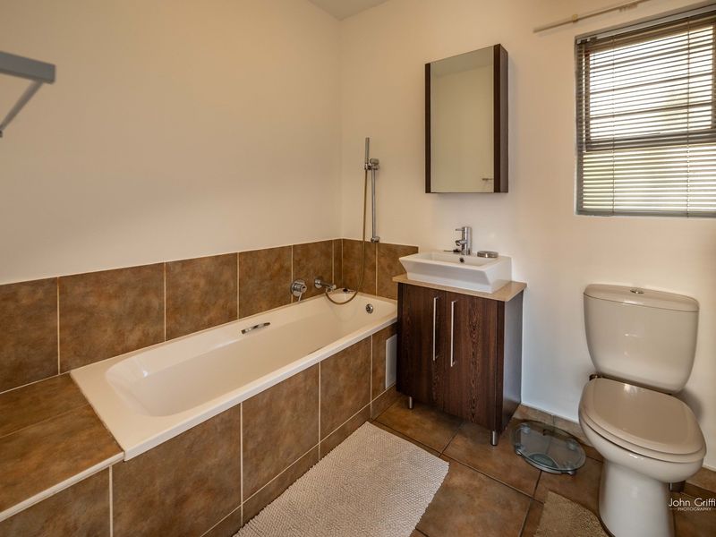 A functional bathroom featuring a built-in bathtub with tiled surround, a vanity cabinet with basin, a mirror cabinet, and a toilet.