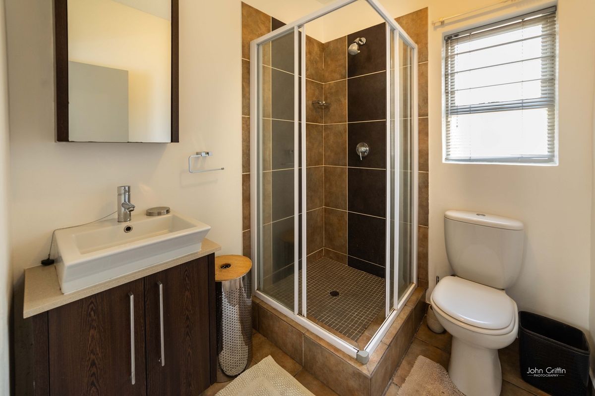 A functional bathroom featuring a corner shower enclosure, vanity cabinet with basin, toilet, and neutral tiled finishes.