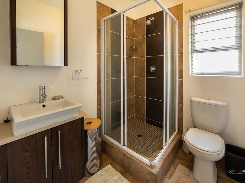 A functional bathroom featuring a corner shower enclosure, vanity cabinet with basin, toilet, and neutral tiled finishes.