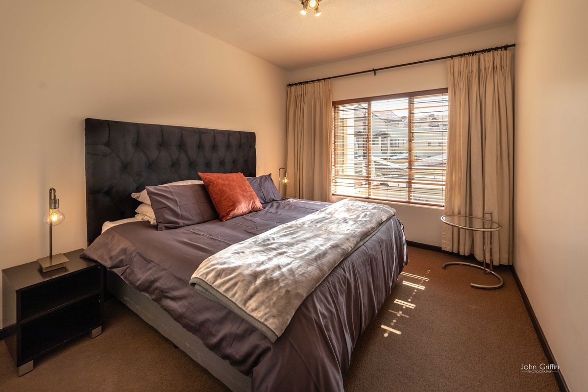 A well-lit bedroom featuring carpeted flooring, window blinds, and curtain tracks, providing a comfortable and functional living space.