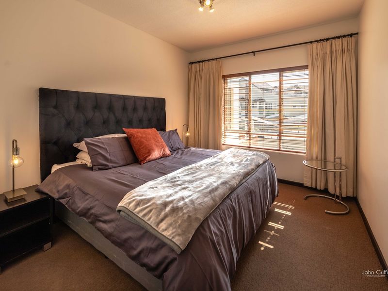 A well-lit bedroom featuring carpeted flooring, window blinds, and curtain tracks, providing a comfortable and functional living space.