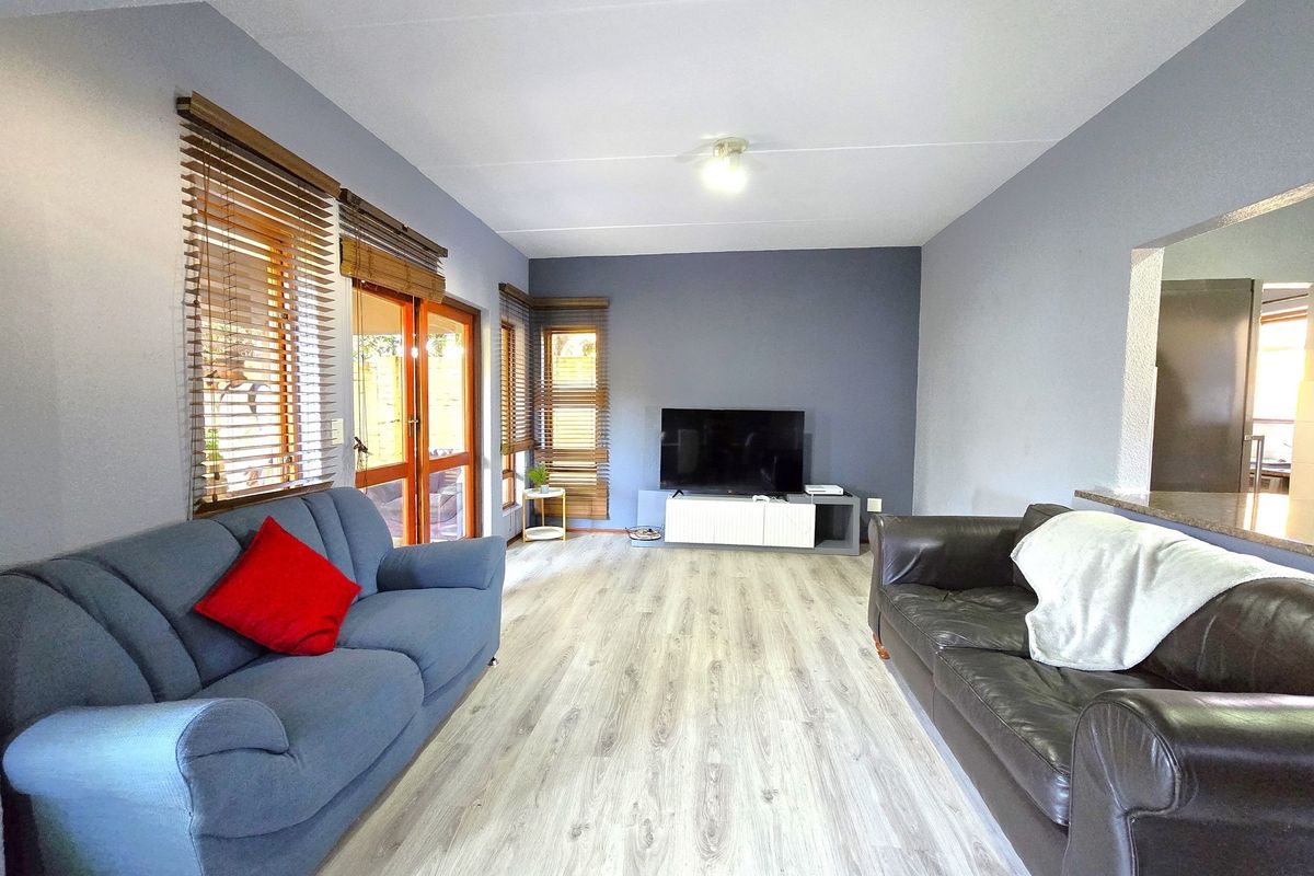 A well-lit living room featuring modern laminate flooring, neutral grey walls, and sliding glass doors providing access to the outdoor area.
