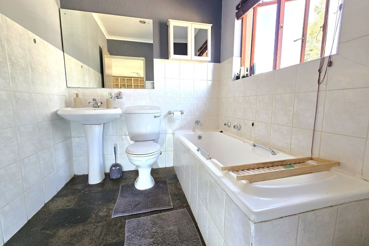 A functional bathroom featuring a pedestal basin, toilet, and bathtub with tiled finishes. The space requires minor maintenance to address missing fixtures and tiles.