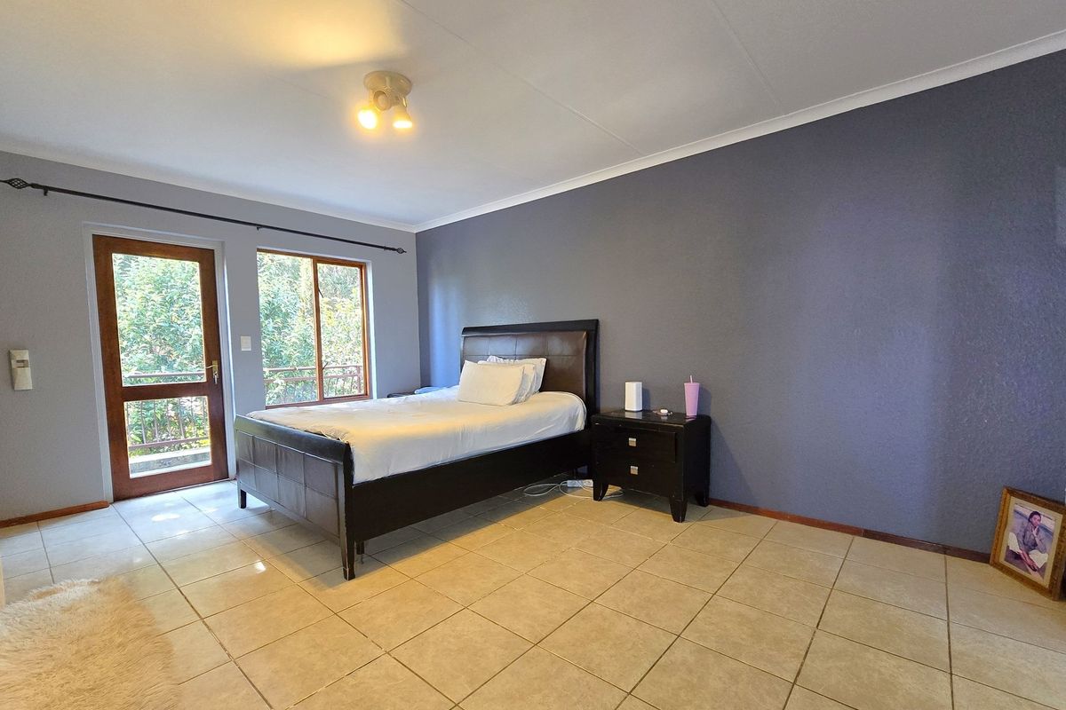 A spacious bedroom featuring tiled flooring, a feature wall, and direct access to an outdoor area through a timber-framed glass door.