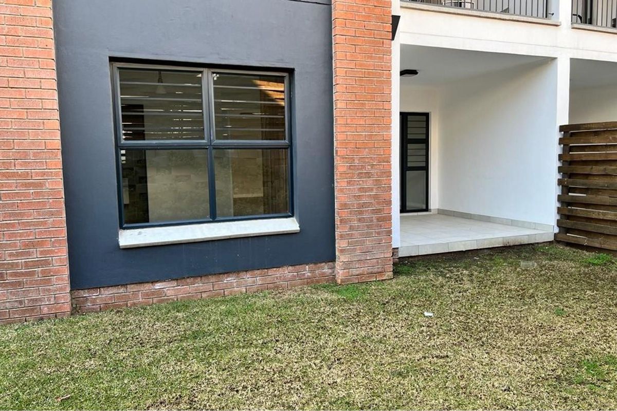 A view of the apartment's rear exterior, featuring a covered patio area, brick and rendered facade, and a small private garden space.