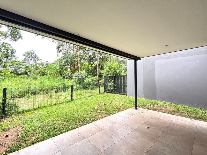 A covered outdoor patio area featuring tiled flooring and a metal support column, overlooking a private grassed garden and surrounding greenery.