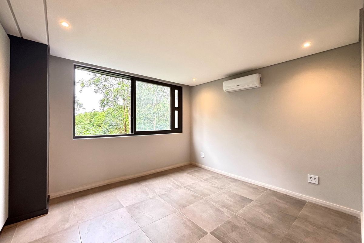 A bright, modern, and empty bedroom featuring neutral tiled flooring, recessed lighting, and a wall-mounted air conditioning unit with large window views.
