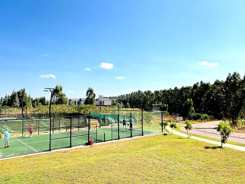Outdoor padel court facility featuring perimeter fencing and integrated floodlights, set within a well-maintained landscaped estate environment.
