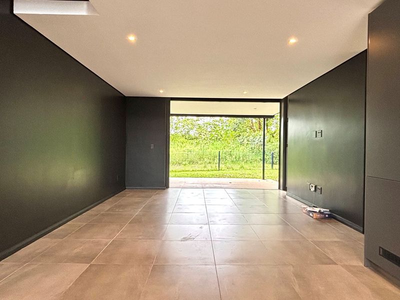 A modern, empty living area featuring dark feature walls, large format floor tiles, recessed lighting, and direct access to an outdoor patio.