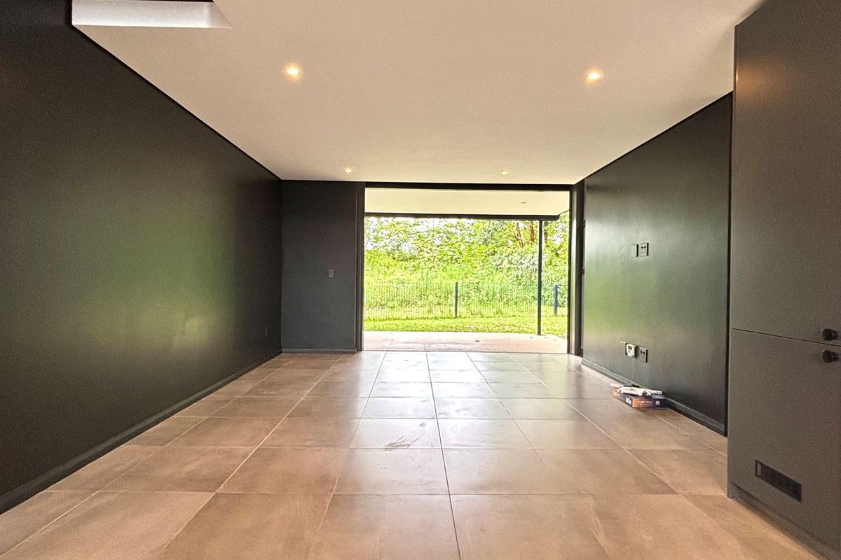 A modern, empty living area featuring dark feature walls, large format floor tiles, recessed lighting, and direct access to an outdoor patio.