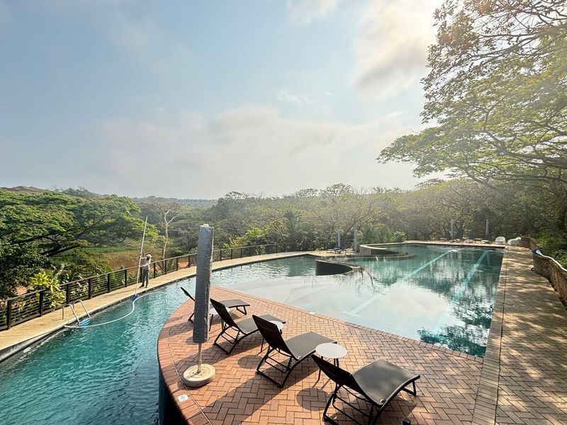 A well-maintained outdoor swimming pool area featuring a brick-paved deck, metal safety railings, and scenic views of the surrounding landscape.